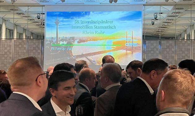 Crowd in the foreground, screen with the event title in the background.