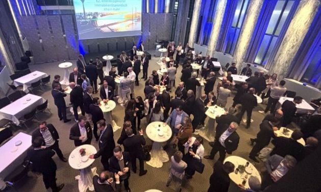 Bird's-eye view, event hall with many people, spread out at standing tables.